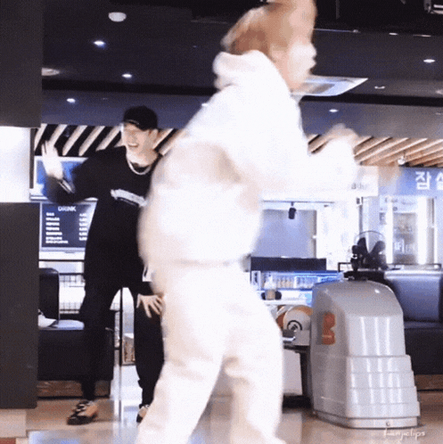 two men are dancing in a bowling alley and one of them is holding a bowling ball .