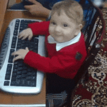 a baby is typing on a keyboard and smiling
