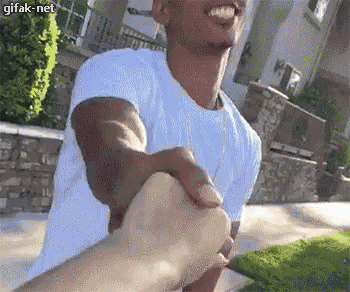 a man in a white shirt is holding another man 's hand while smiling .
