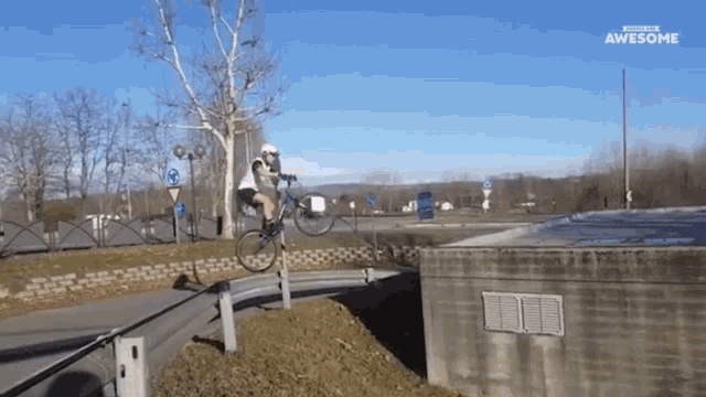 a man is riding a bike over a concrete wall and the words awesome are on the bottom of the screen