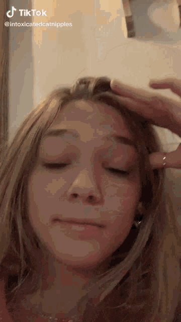 a young girl is making a funny face with her eyes closed and her hand on her head .