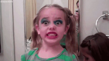 a little girl with makeup on her face is looking at herself in the mirror .