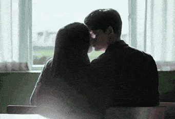 a man and woman are kissing in front of a window .
