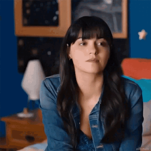 a woman wearing a denim jacket is sitting on a bed .