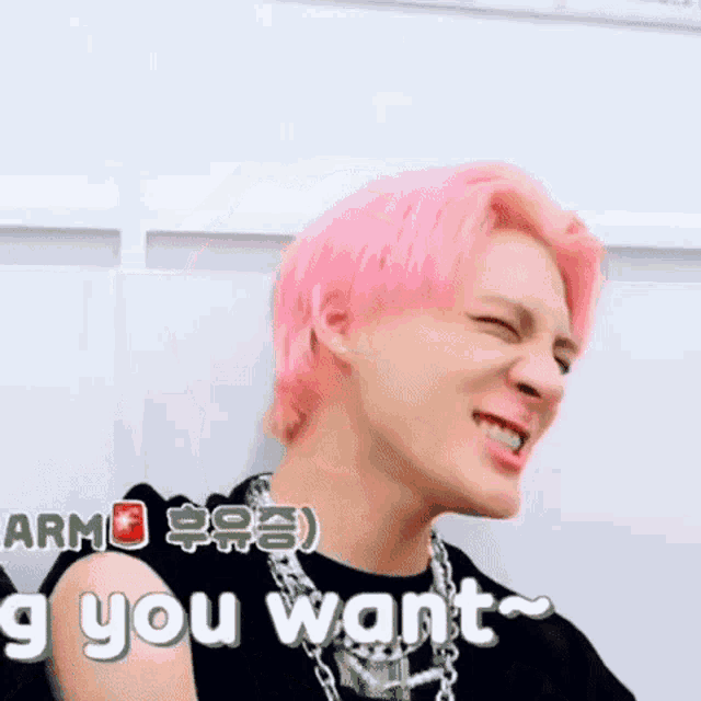 a man with pink hair is making a funny face while wearing a black shirt and a necklace .