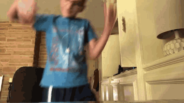 a boy in a blue shirt is dancing in front of a fireplace