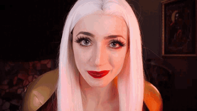 a woman with long white hair and red lipstick is looking at the camera