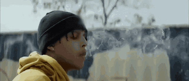 a man wearing a black beanie and a yellow hoodie is smoking a cigarette .