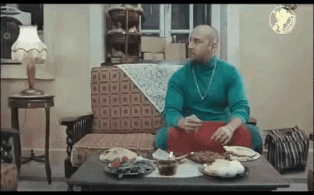 a man in a green turtleneck is sitting at a table with food on it