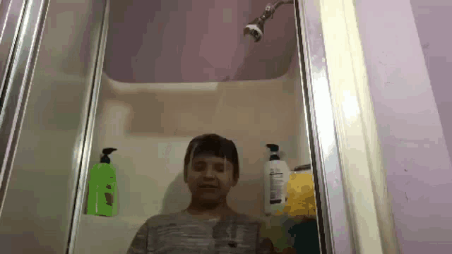 a young boy is taking a shower in a bathroom with a shower head .
