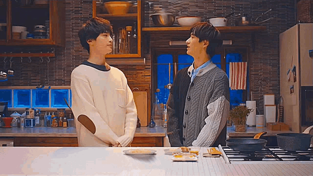 two men standing next to each other in a kitchen talking