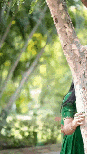 a woman in a green dress leans against a tree trunk
