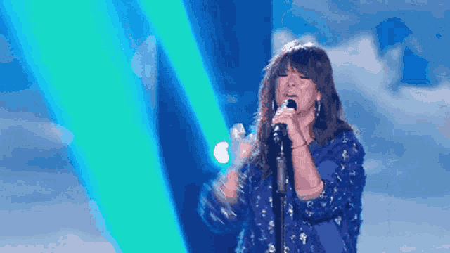 a woman singing into a microphone in front of a blue background