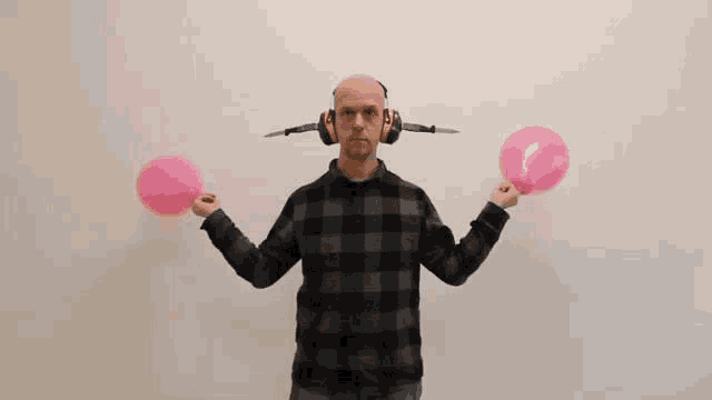 a bald man wearing headphones is holding two pink balloons in his hands .