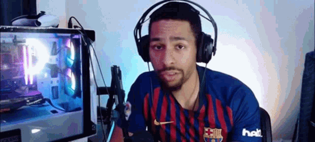 a man wearing headphones and a fc barcelona shirt is sitting in front of a computer monitor .