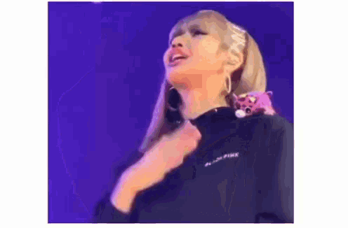 a woman is standing on a stage with a stuffed animal on her shoulder and holding her chest .