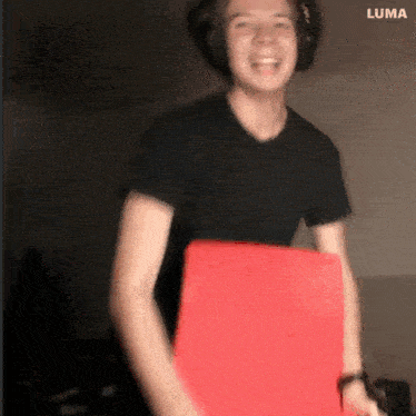 a man wearing headphones and a black shirt is holding a red box ..