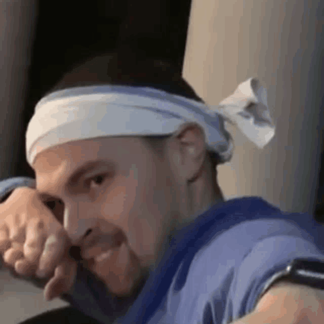a man wearing a headband and a blue shirt is smiling and looking at the camera .