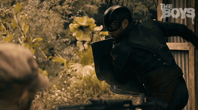 a man in a superhero costume is holding a shield in front of a sign that says ' the boys '