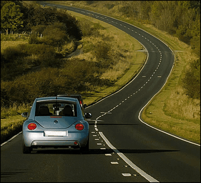 a blue volkswagen beetle is driving down a road