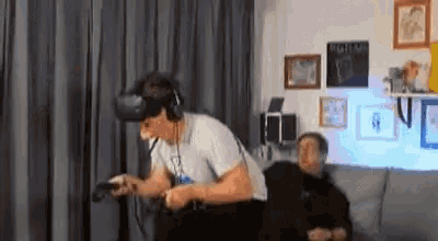 a man wearing a virtual reality headset is playing a video game while another man watches .