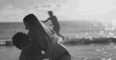 a black and white photo of a man carrying a woman on the beach .
