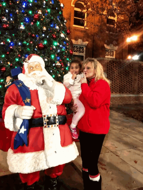a woman is holding a little girl in front of a santa claus statue