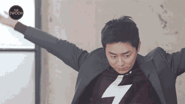 a man with his arms outstretched is wearing a sweater with a lightning bolt on it and a suit jacket