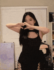 a woman is making a heart shape with her hands while wearing a black dress .