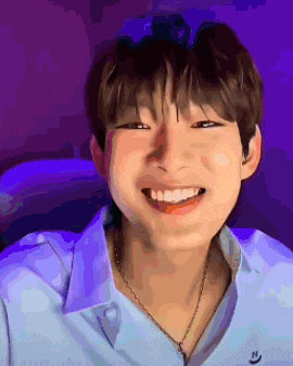 a young man wearing a blue shirt and necklace is smiling .