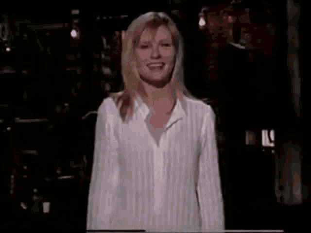 a woman in a white striped shirt is standing in a dark room and smiling .