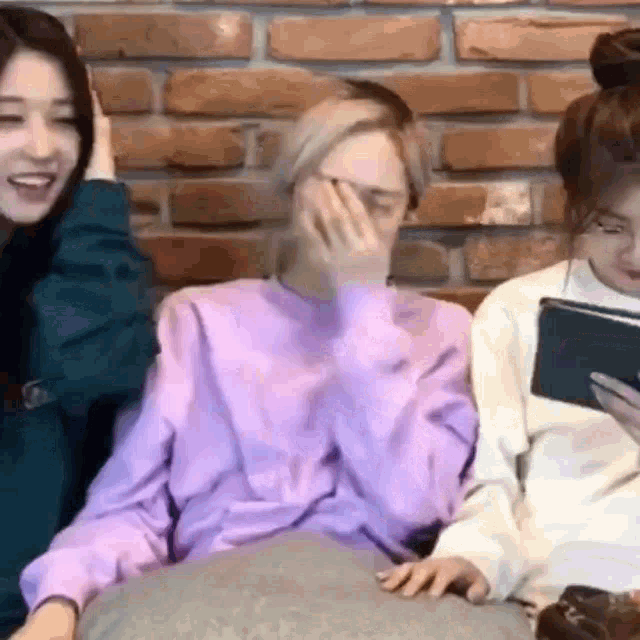 a group of women are sitting next to each other on a couch laughing and looking at a tablet .