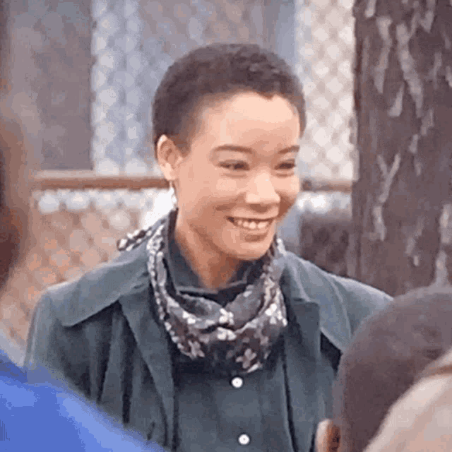 a woman wearing a scarf and a jacket is smiling while standing next to a group of people .