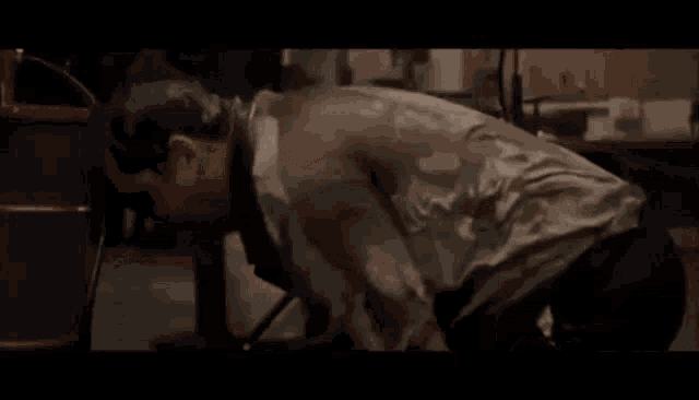 a man in a dirty shirt is kneeling down in front of a red barrel in a dark room .