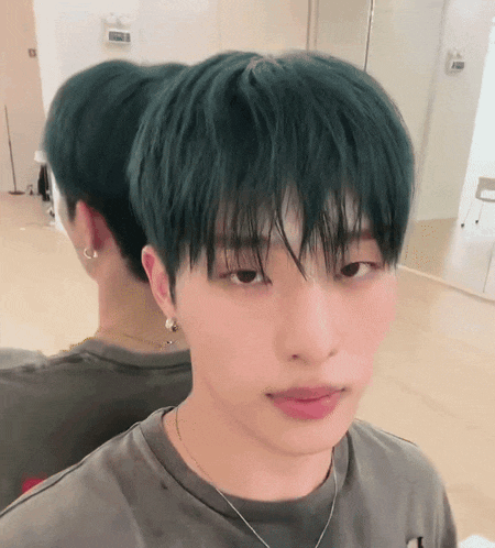 a young man with green hair is looking at his reflection in the mirror