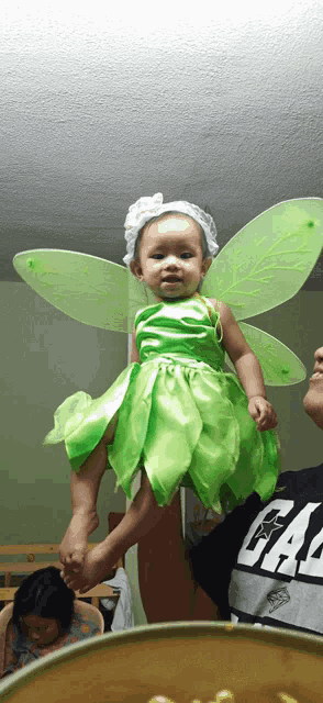 a baby in a tinkerbell costume is being held by a man wearing a gap shirt