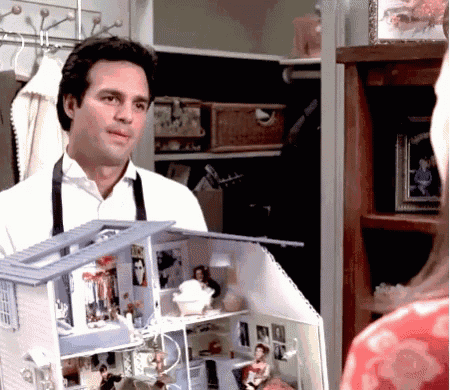 a man in an apron is holding a doll house in a closet