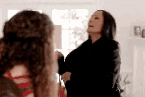 a woman in a black jacket is dancing in a room with other women .