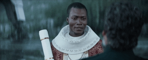 a man in a white robe is talking to another man in a dark room