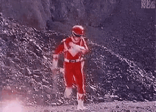 a red power ranger is running down a dirt road in front of a mountain .