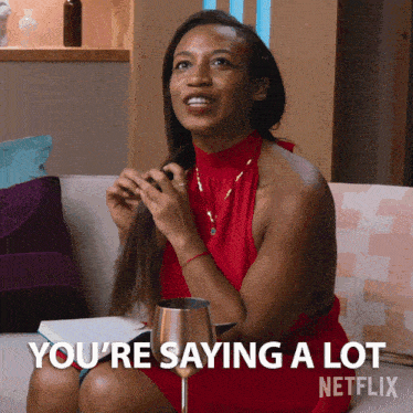 a woman in a red dress is sitting on a couch with a glass of wine and says you 're saying a lot