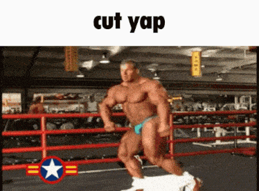 a muscular man in a blue bikini is running in a boxing ring with the words cut yap above him