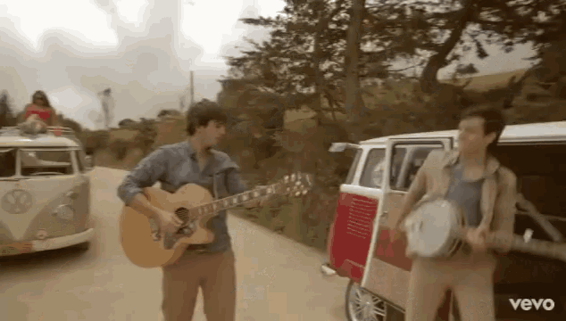 a man is playing a guitar and a man is playing a banjo in front of a vw van .