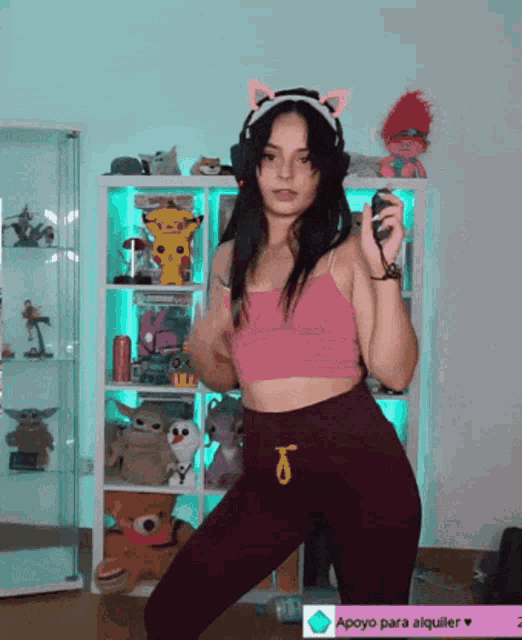 a woman in a pink top and purple pants stands in front of a shelf with stuffed animals