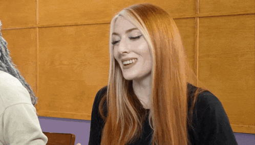 a woman with long red hair is smiling and wearing a black top