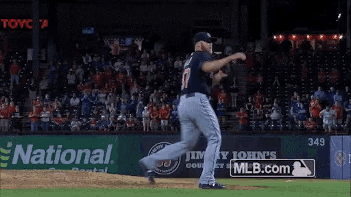 a man wearing an indians jersey is dancing in front of a mlb.com sign