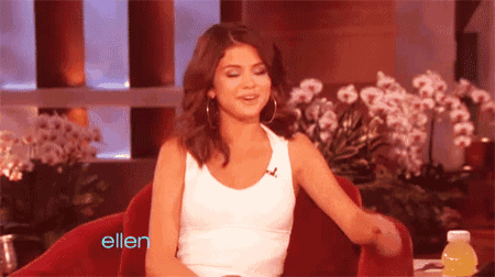 a woman in a white tank top is sitting in a red chair in front of a bottle of ellen