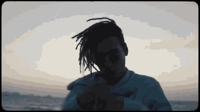 a man with dreadlocks wearing sunglasses is standing on the beach