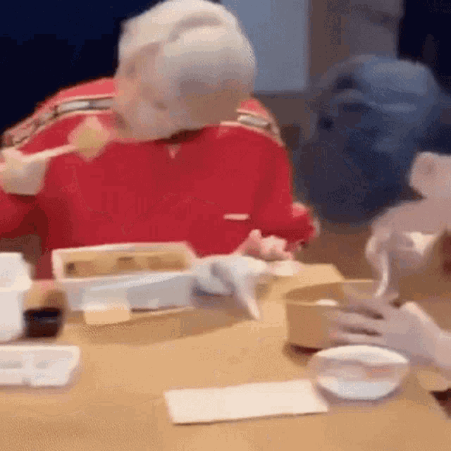 a woman in a red sweater is sitting at a table eating food .