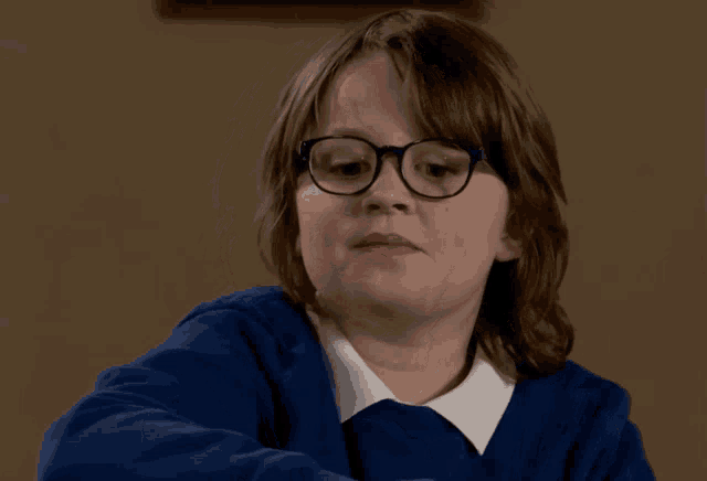 a young girl wearing glasses and a blue sweater looks at the camera
